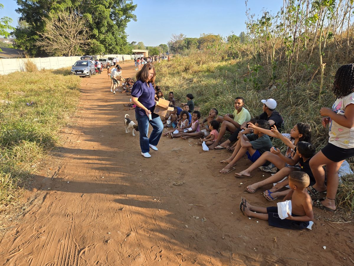 A volunteer serving food packages to children seated along the road