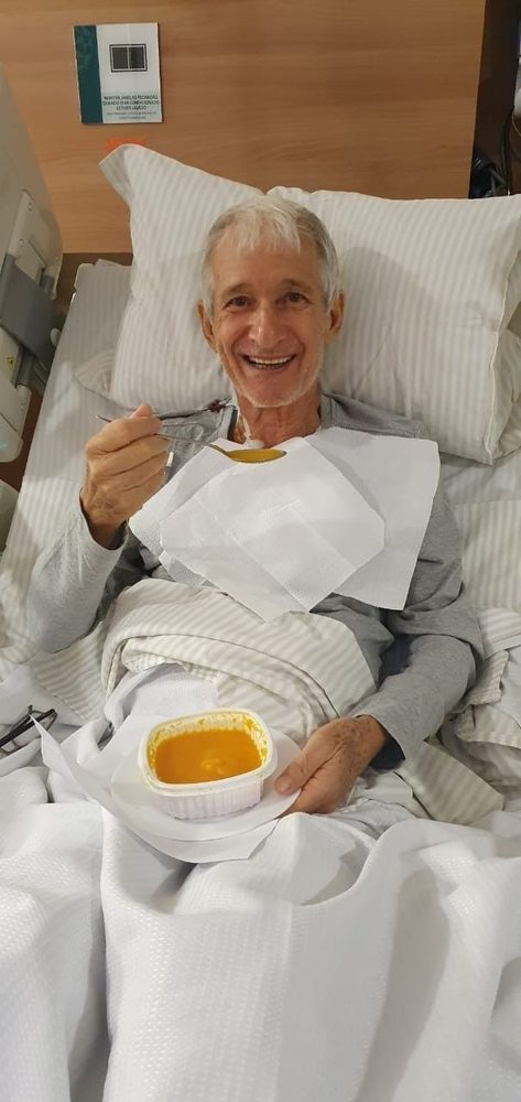 The brother-in-law in 2025, smiling broadly while eating soup in his hospital bed